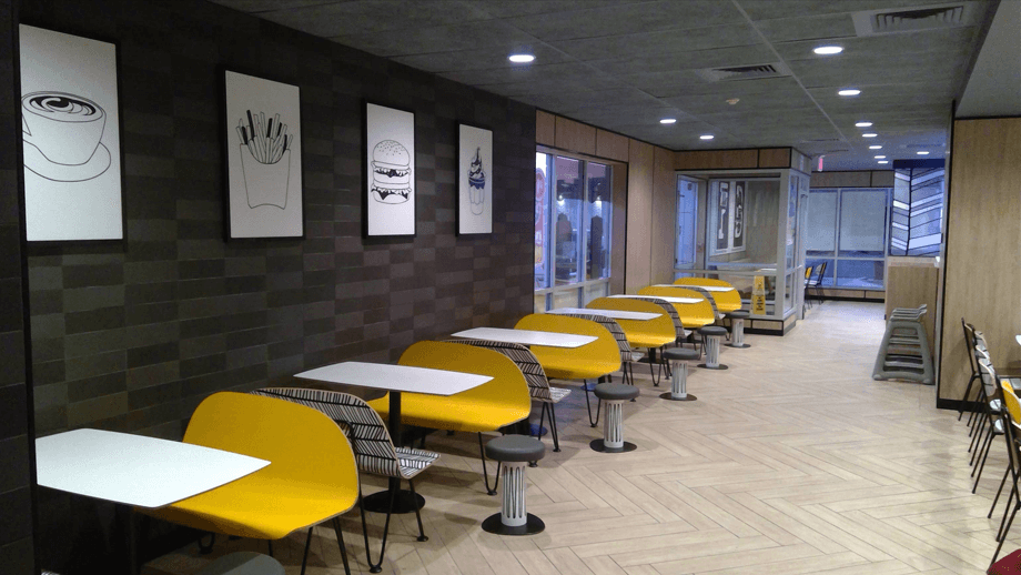 Indoor image of McDonalds showing the dining area with yellow benches and white tables.