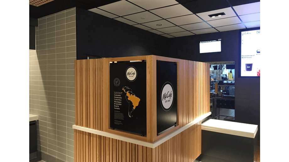 Indoor image of McDonalds showing wooden backboard and two black McCafe signs.