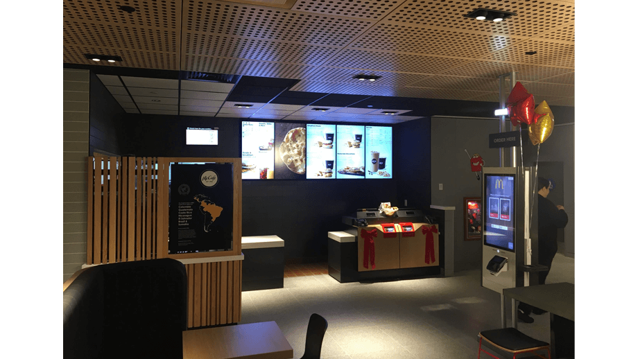 Indoor image of McDonalds showing cashier area, order kiosk, and menu screens.