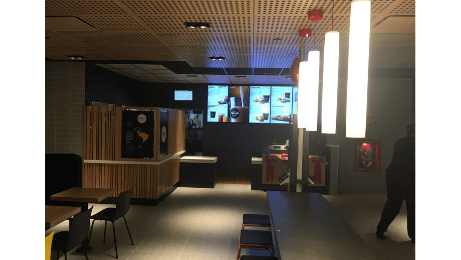 Indoor image of McDonalds showing dining area main table, stools, and menu screens.